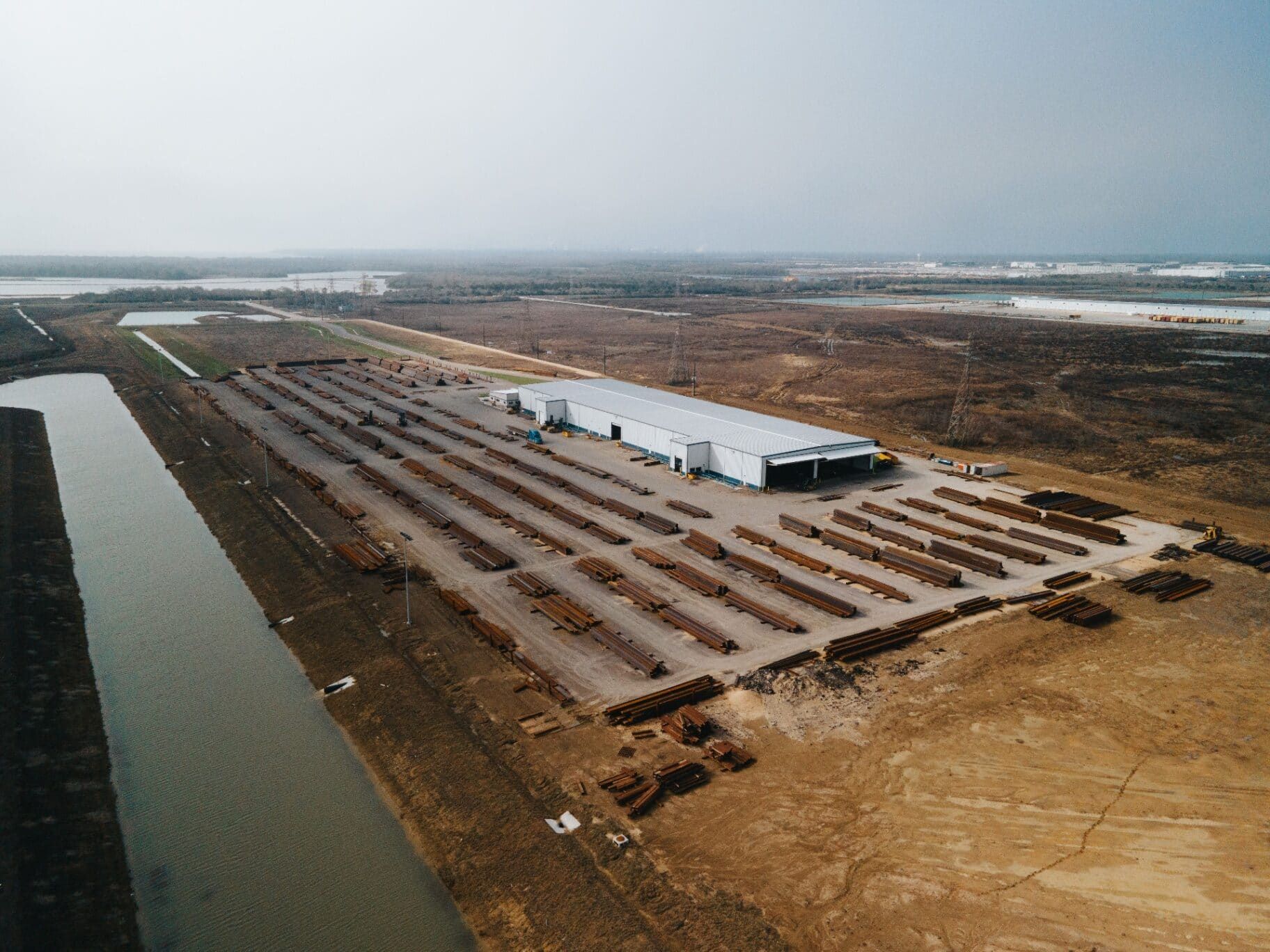 Aerial view of the Brown Strauss steel yard with rows of stacked beams beside the canal
