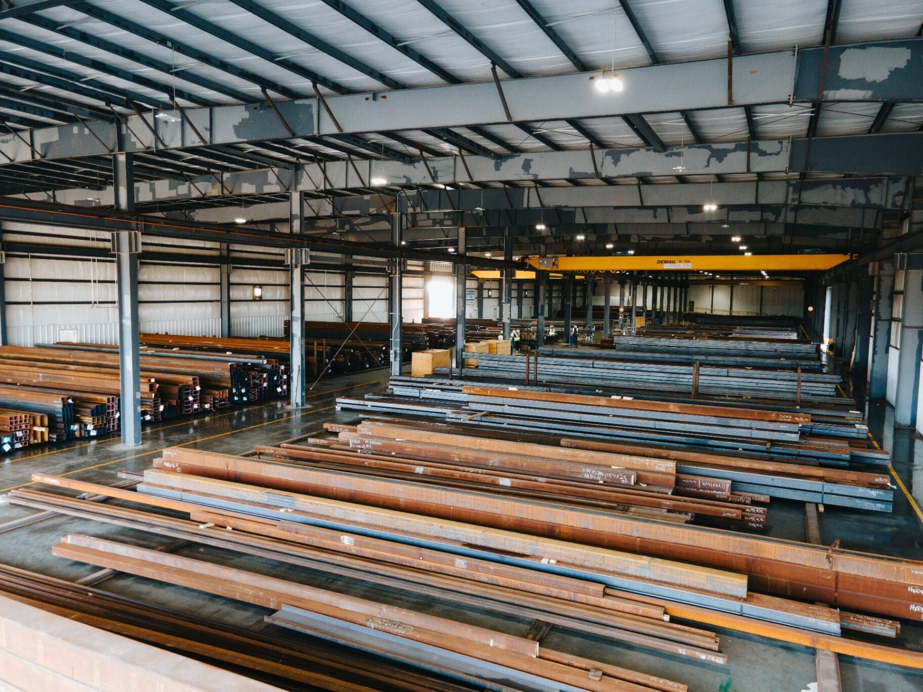Wide interior view of the Brown Strauss warehouse showing organized steel inventory and Demag cranes
