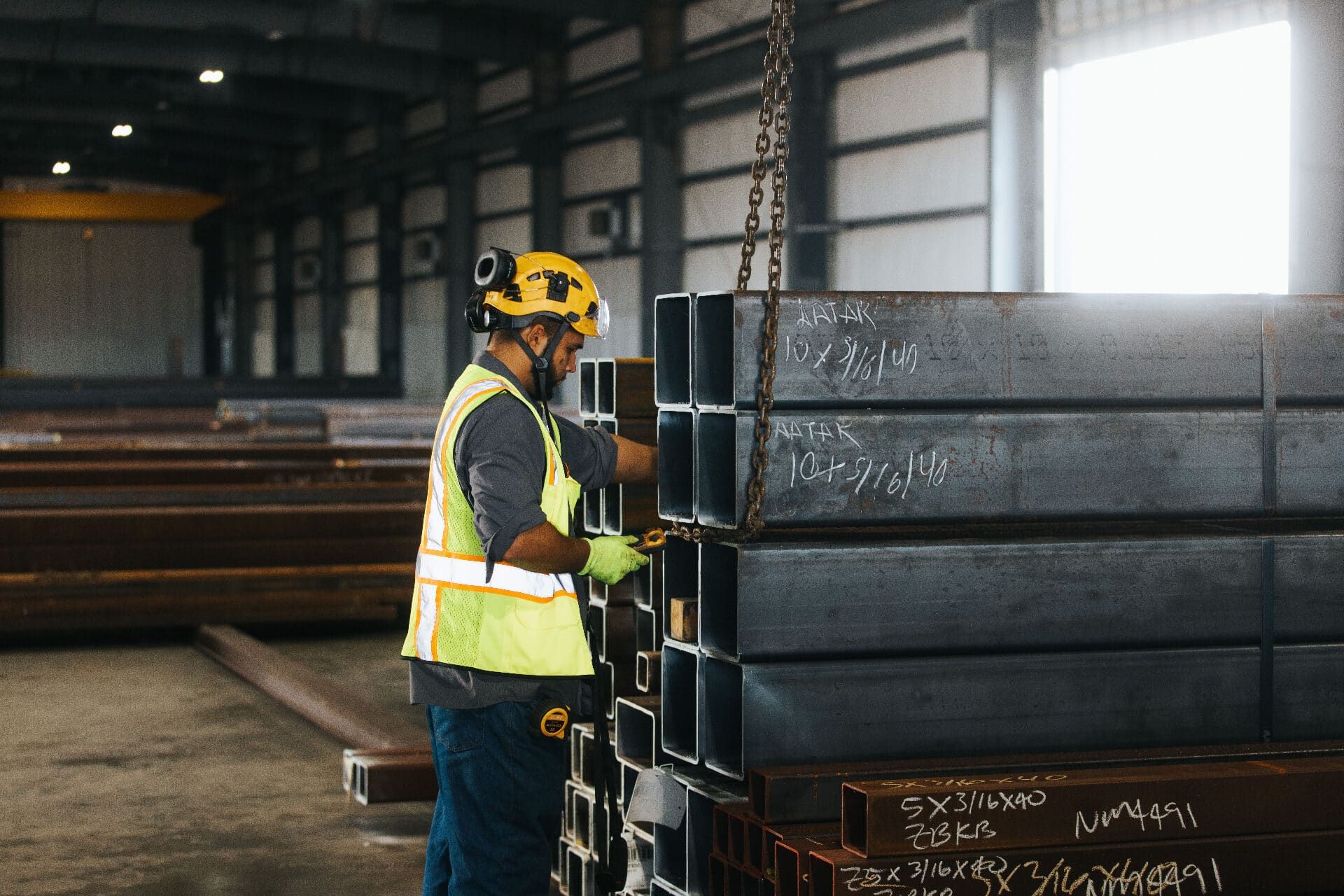 Brown Strauss Steel worker rigging chains to a stack of square steel tubing